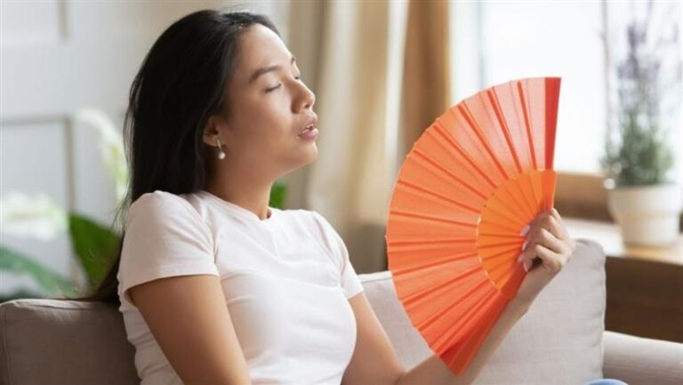 Woman Using Hand Fan to Cool Down in a Bright Living Room