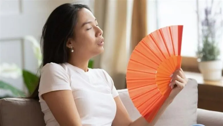 Woman Using Hand Fan to Cool Down in a Bright Living Room