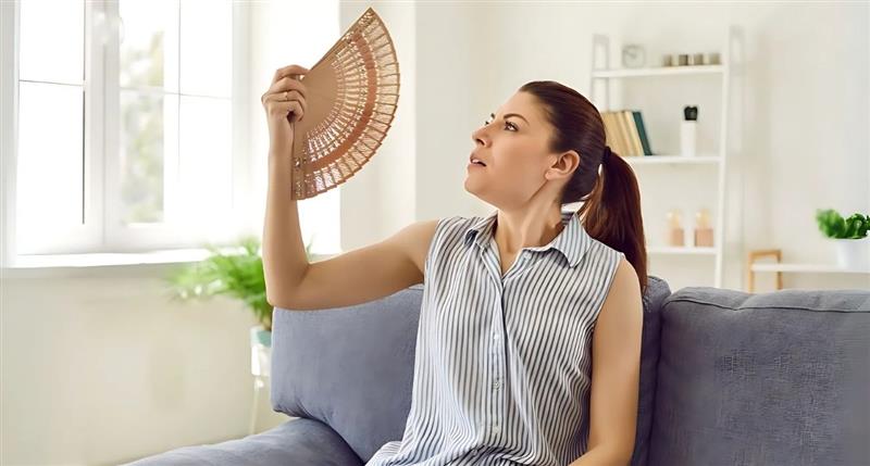Woman Using Hand Fan to Cool down in Living Room