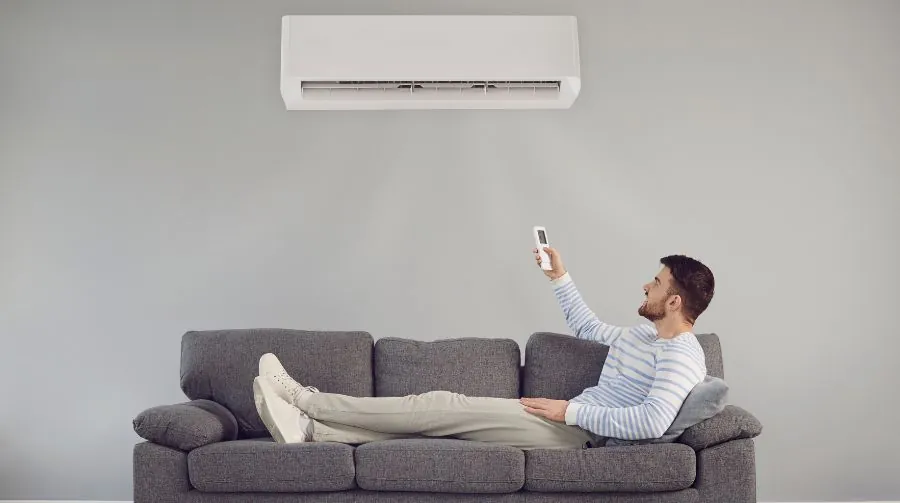 Man Adjusting A Wall-mounted Ac Unit With A Remote
